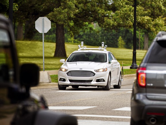 A white Ford Fusion sedan with self-driving sensors on a suburban street