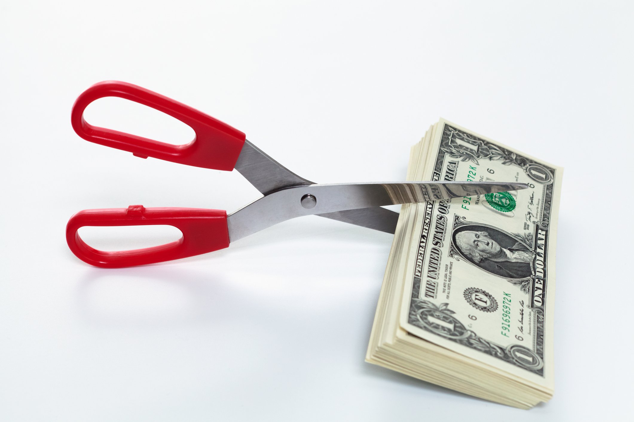 A pair of scissors are set to cut a stack of dollar bills.
