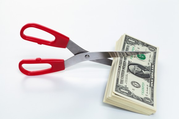 A pair of scissors are set to cut a stack of dollar bills.