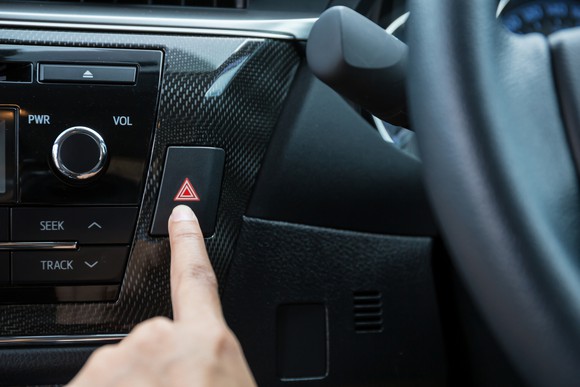 A driver reaches for the hazard-light switch on the dashboard.