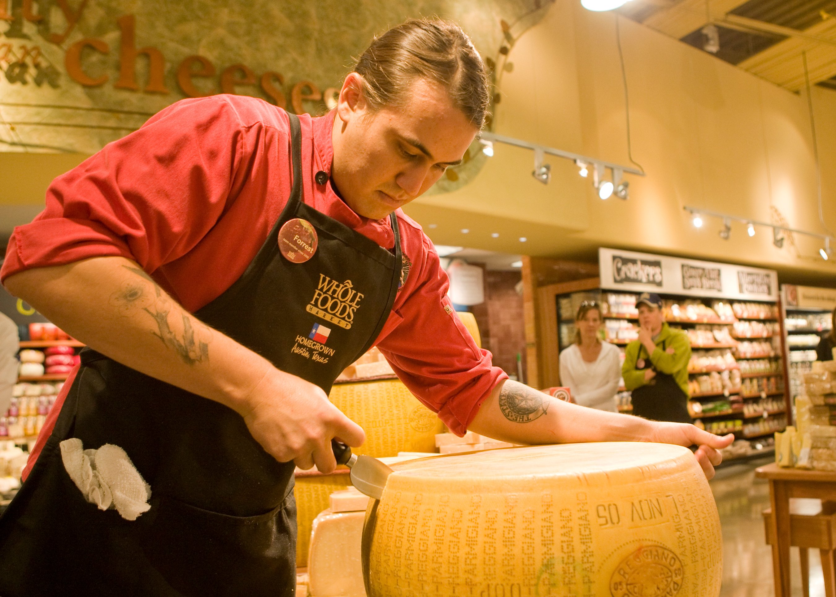 A Whole Foods employee slices a wheel of cheese.