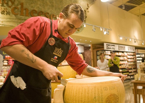 A Whole Foods employee slices a wheel of cheese.