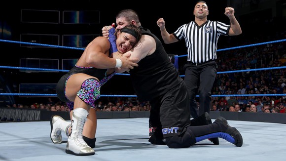 Two wrestlers engage in the ring at a WWE match, as a referee looks on.