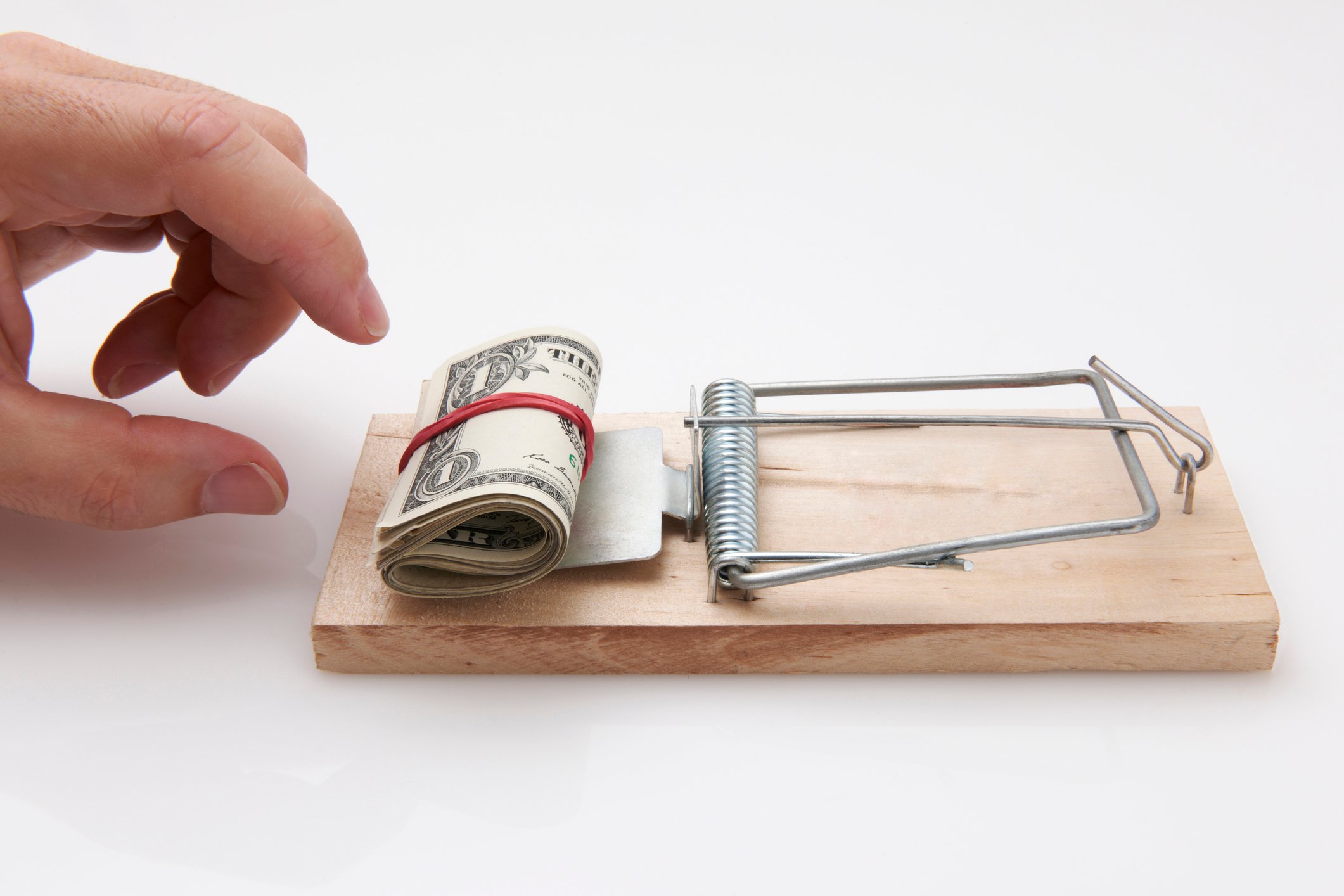 A hand reaches toward money on a mousetrap.