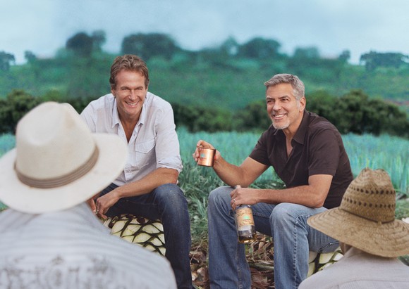 George Clooney and business partner sitting at the edge of an agave field in Mexico, enjoying a batch of tequila with farm workers.