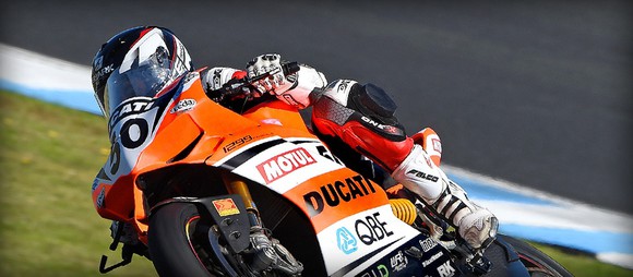 A racer on the track makes a turn on a Ducati racing motorcycle.