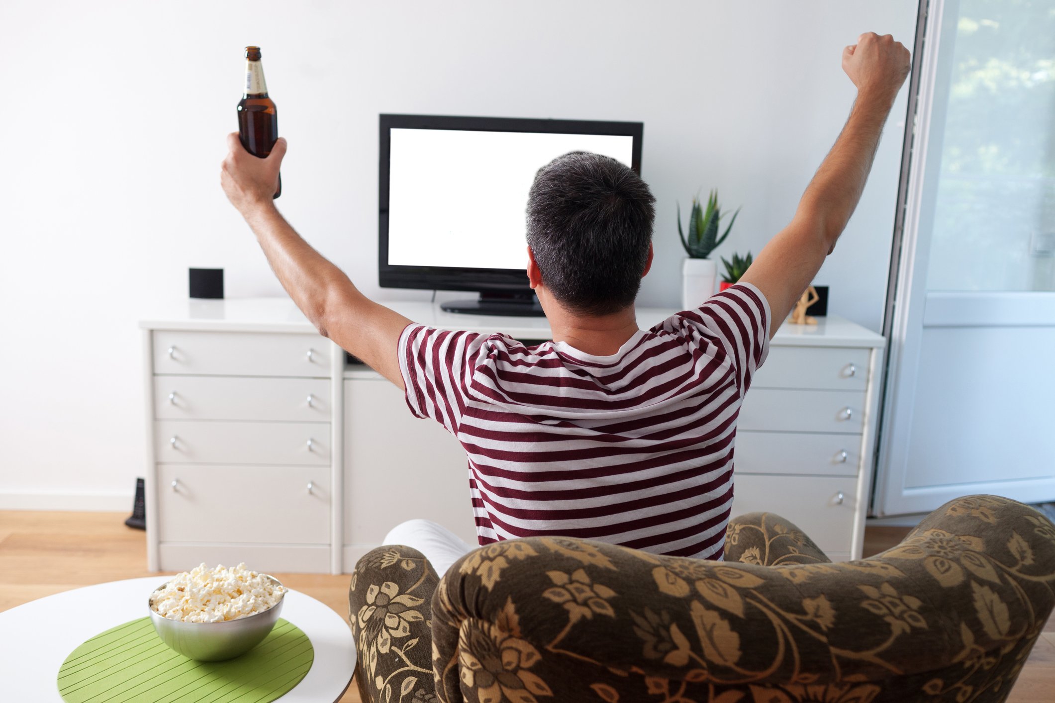 A young man makes the touchdown sign as he watches TV.