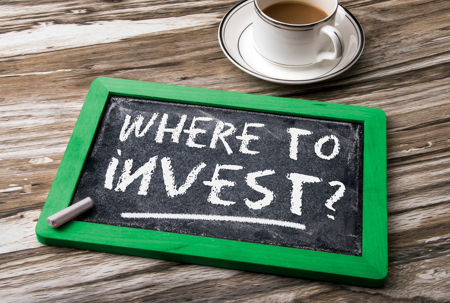 Slate on table next to coffee cup with "where to invest" written in chalk.
