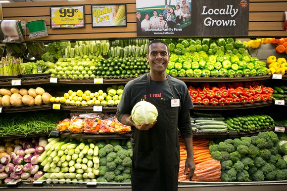 A Kroger employee holding a head of cabbage in the produce aisle.