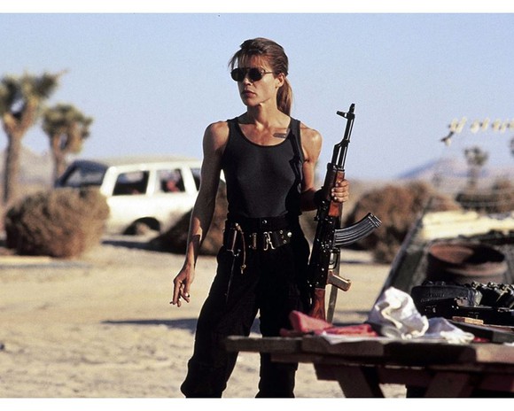 Actress Lilnda Hamilton portraying Sarah Connor, holding a gun in a desert.
