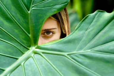 Young Woman Hiding Behind Large Leaves