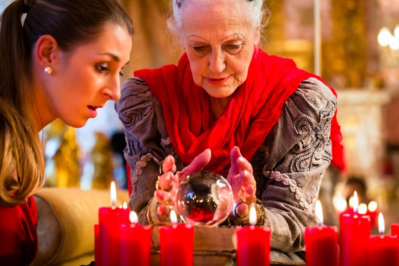 Two women: elderly soothsayer with crystal ball, and young client looking surprised.