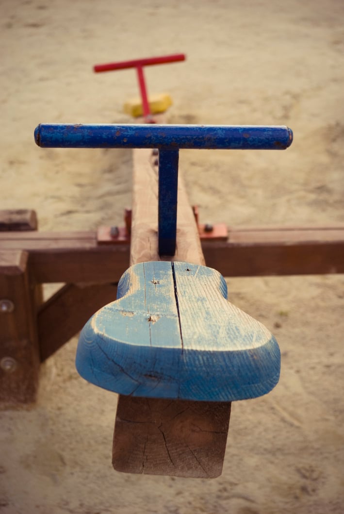 Wooden playground seesaw painted in blue and red.