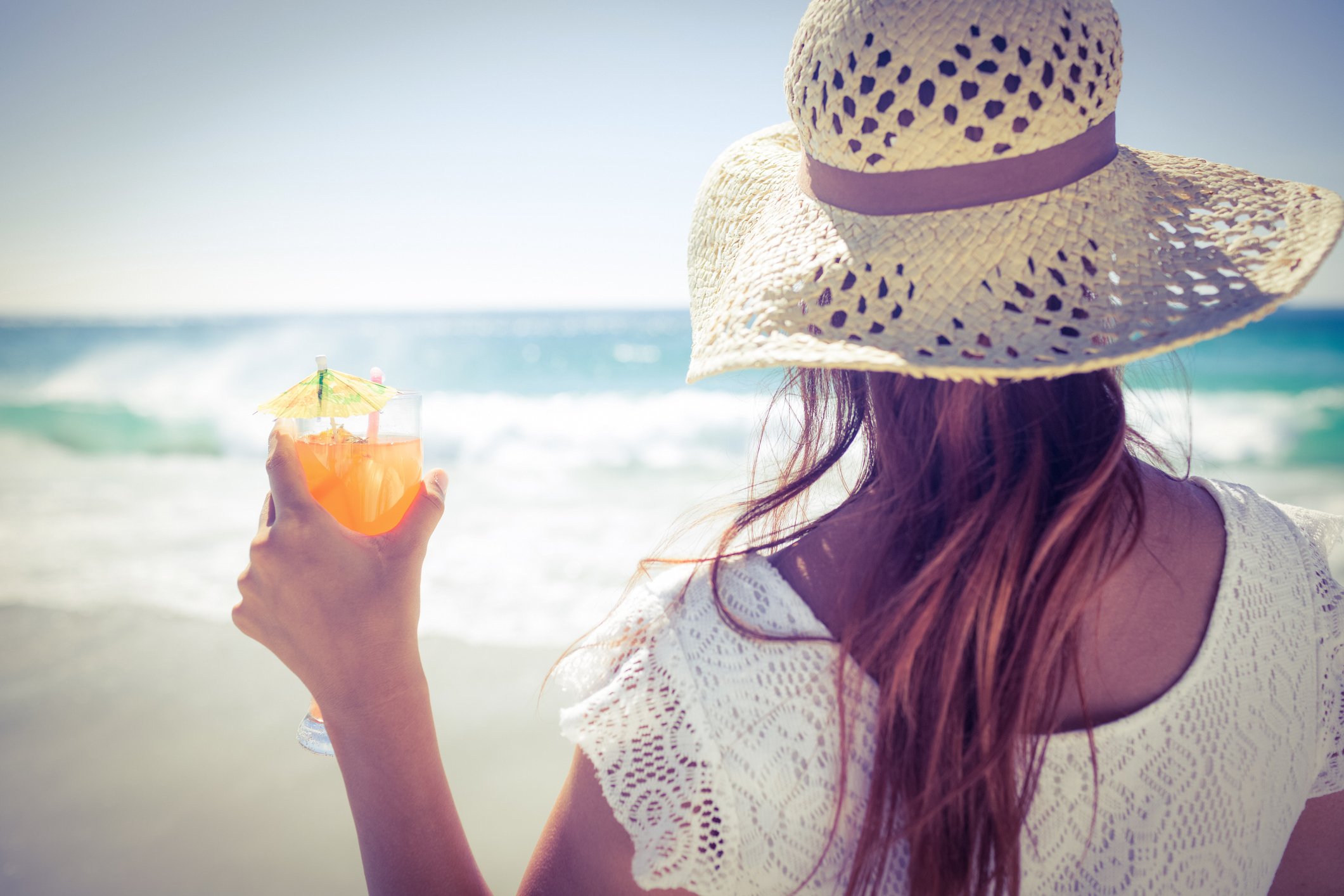 Woman wearing a straw hat drinking a cocktail on a beach