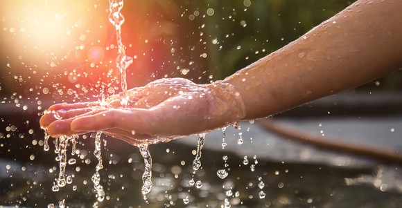 A hand catches falling water in front of the setting sun.