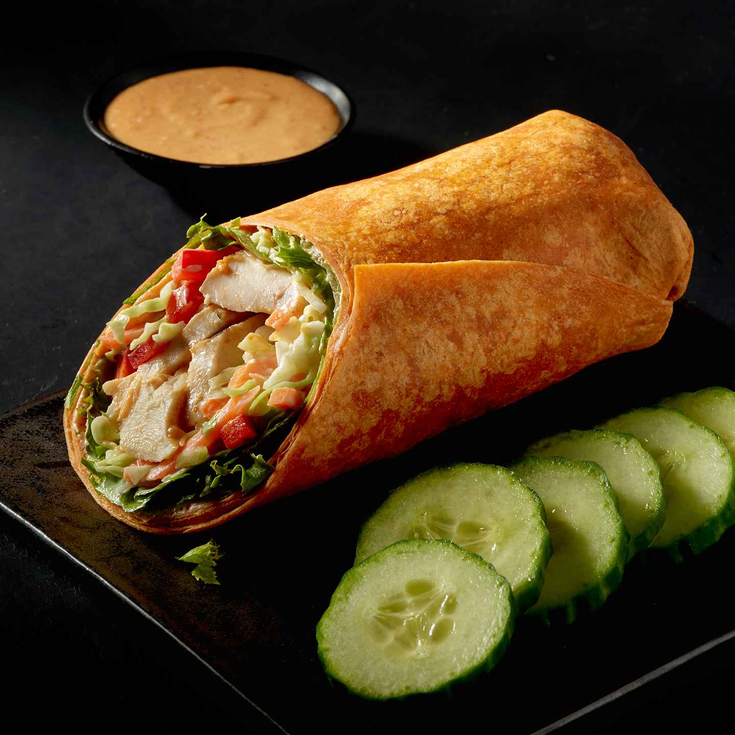 Thai chicken wrap with cucumber slices on the side.