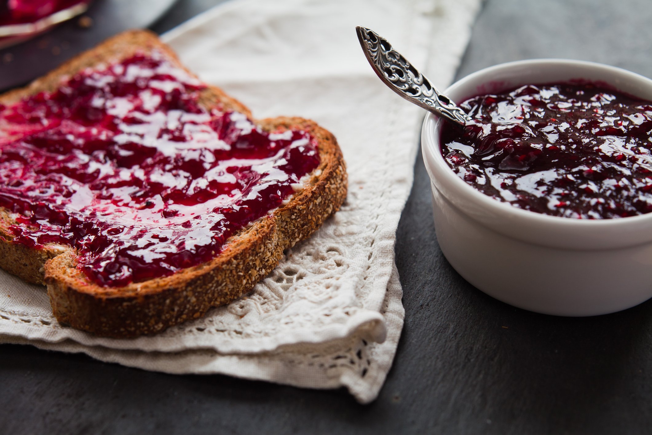 A piece of jelly toast sits on a napkin next to a bowl of jelly. 