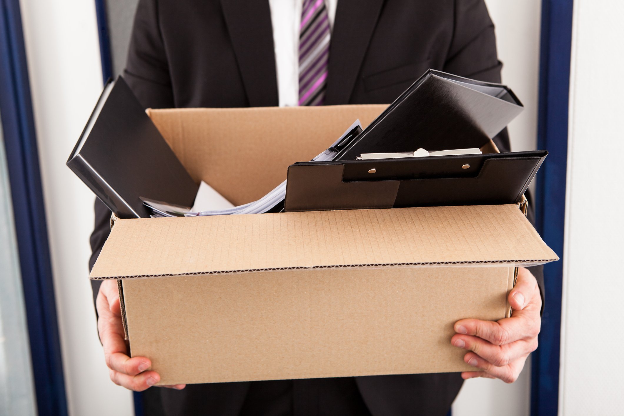 Man in suit walking with cardboard box full of belongings.