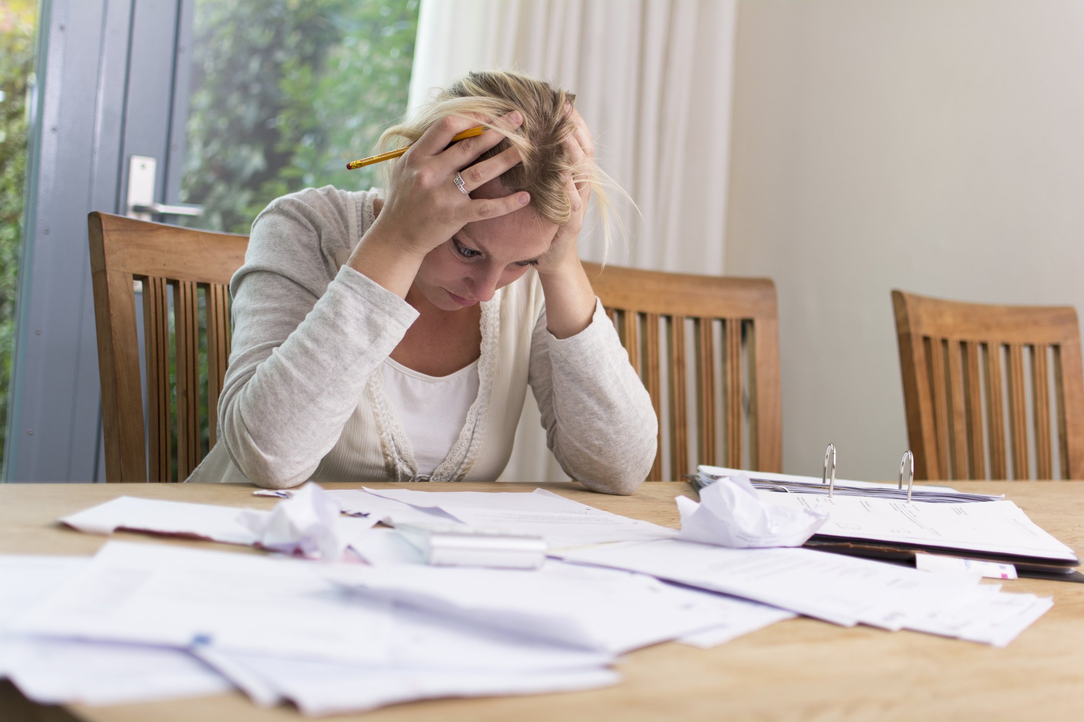 Unhappy woman at desk with papers around and her head in her hands.