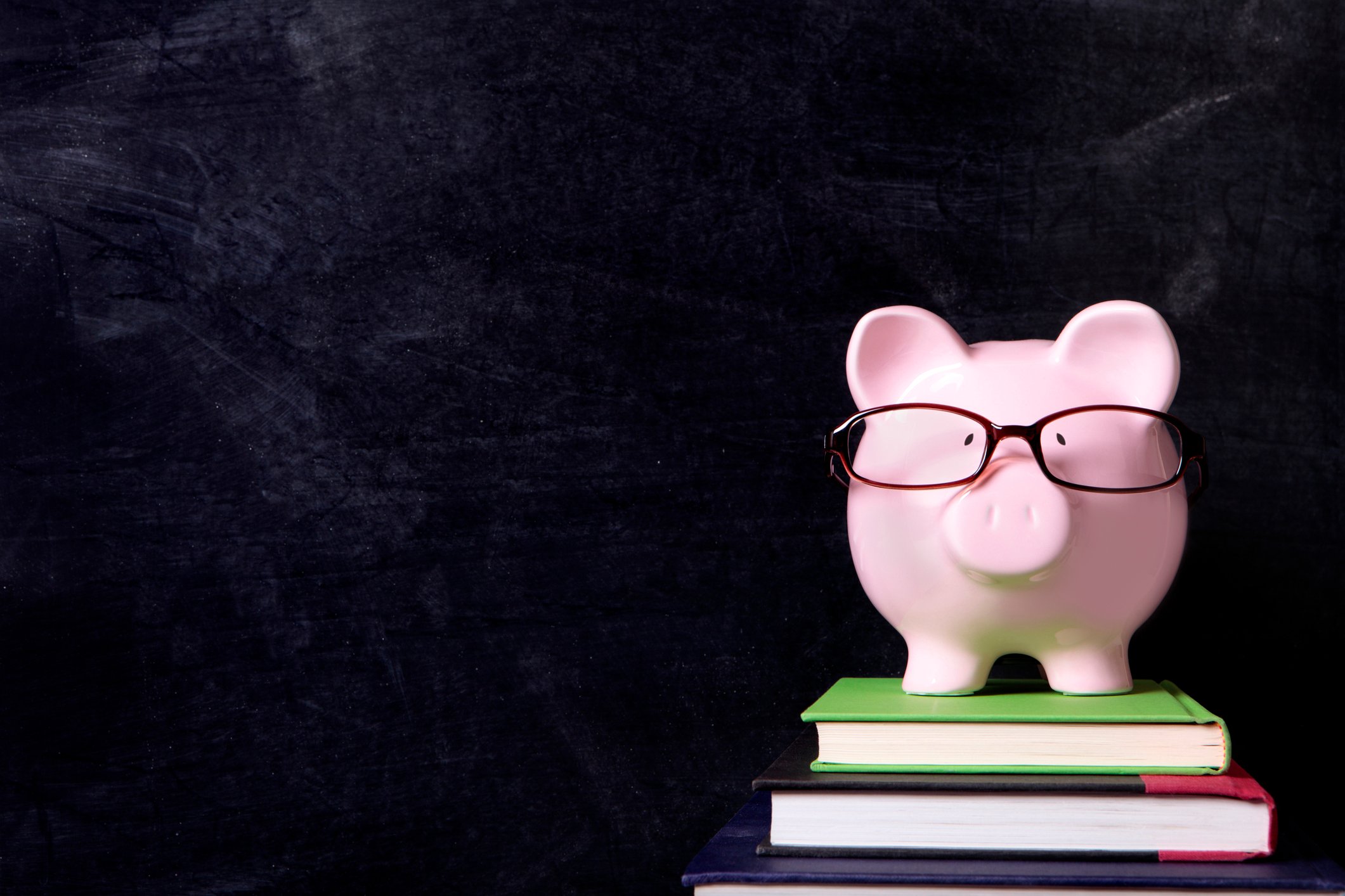 A piggybank wearing glasses and sitting on a few books.
