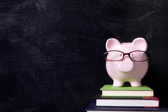 A piggybank wearing glasses and sitting on a few books.