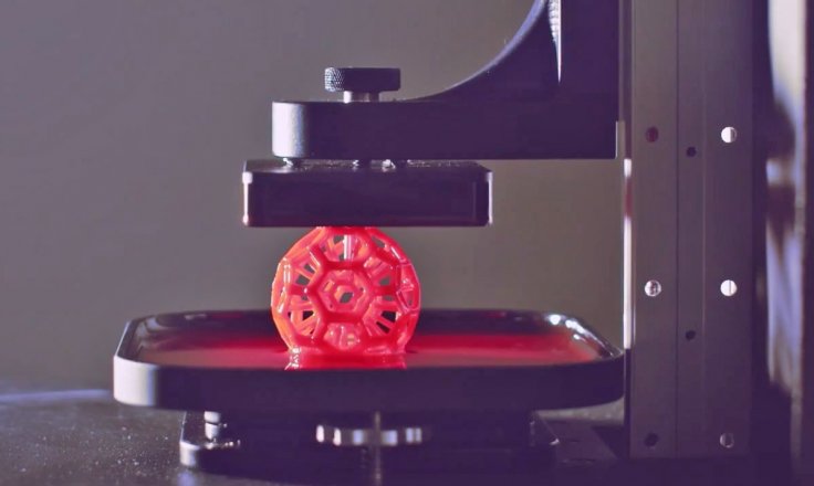 A spherical polymer object built in a soccer ball pattern of hexagons and pentagons, rising from a pool of resin in a Carbon 3D printer.