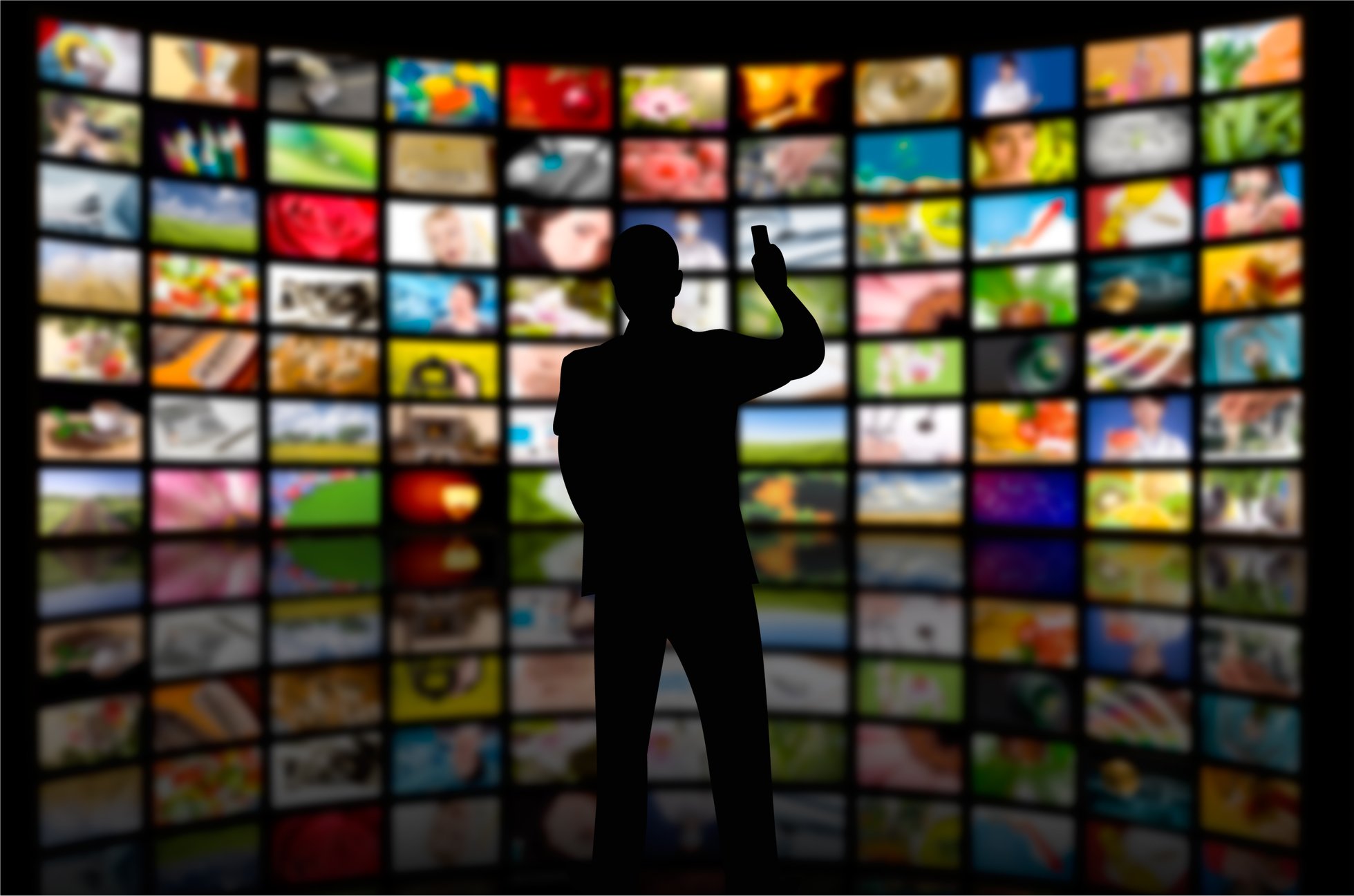 A man stands in front of a wall of monitors.