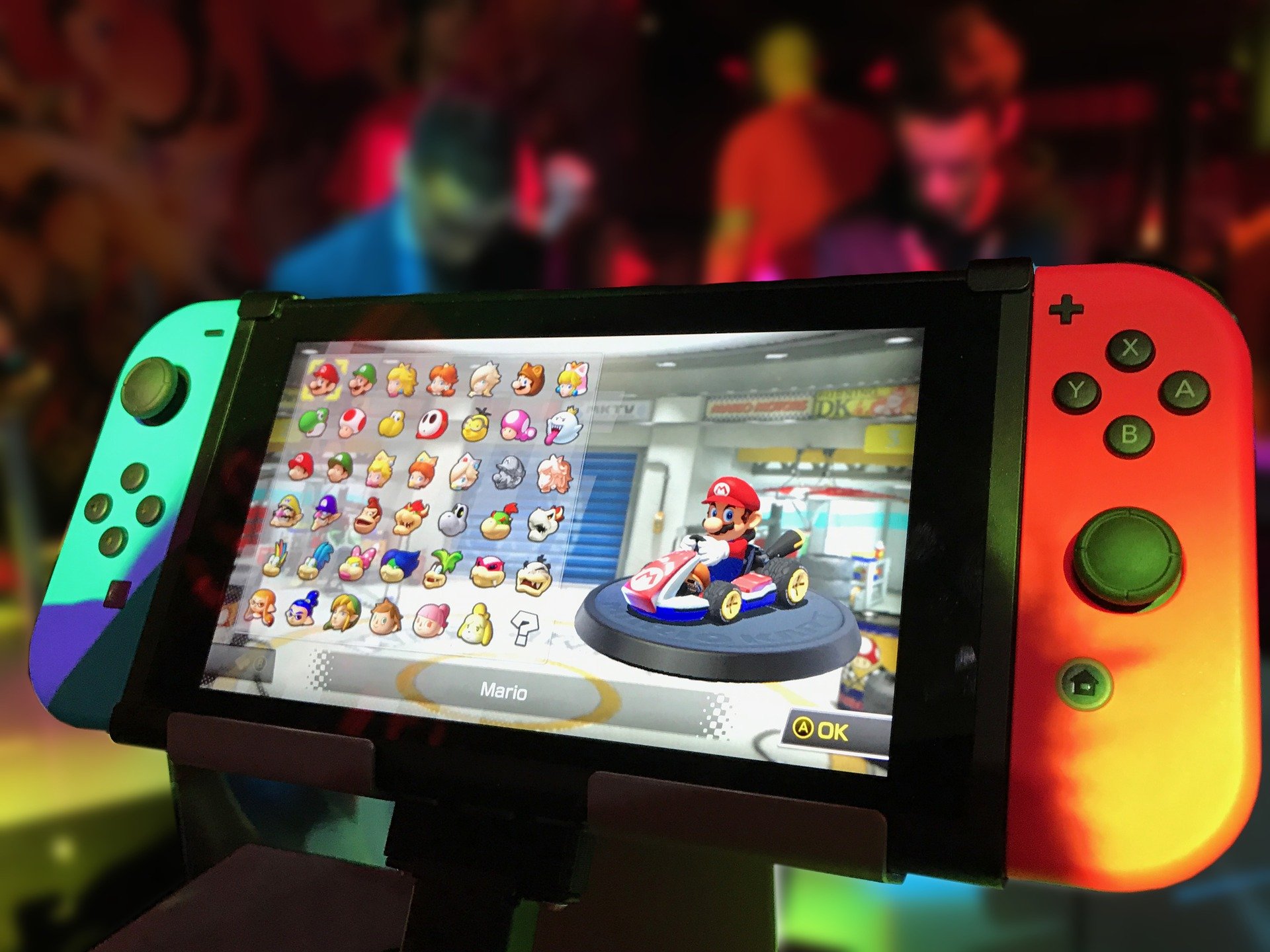 Nintendo Switch with red and neon blue controllers attached to the side of the devices screen, powered on with a Mario game on the screen.