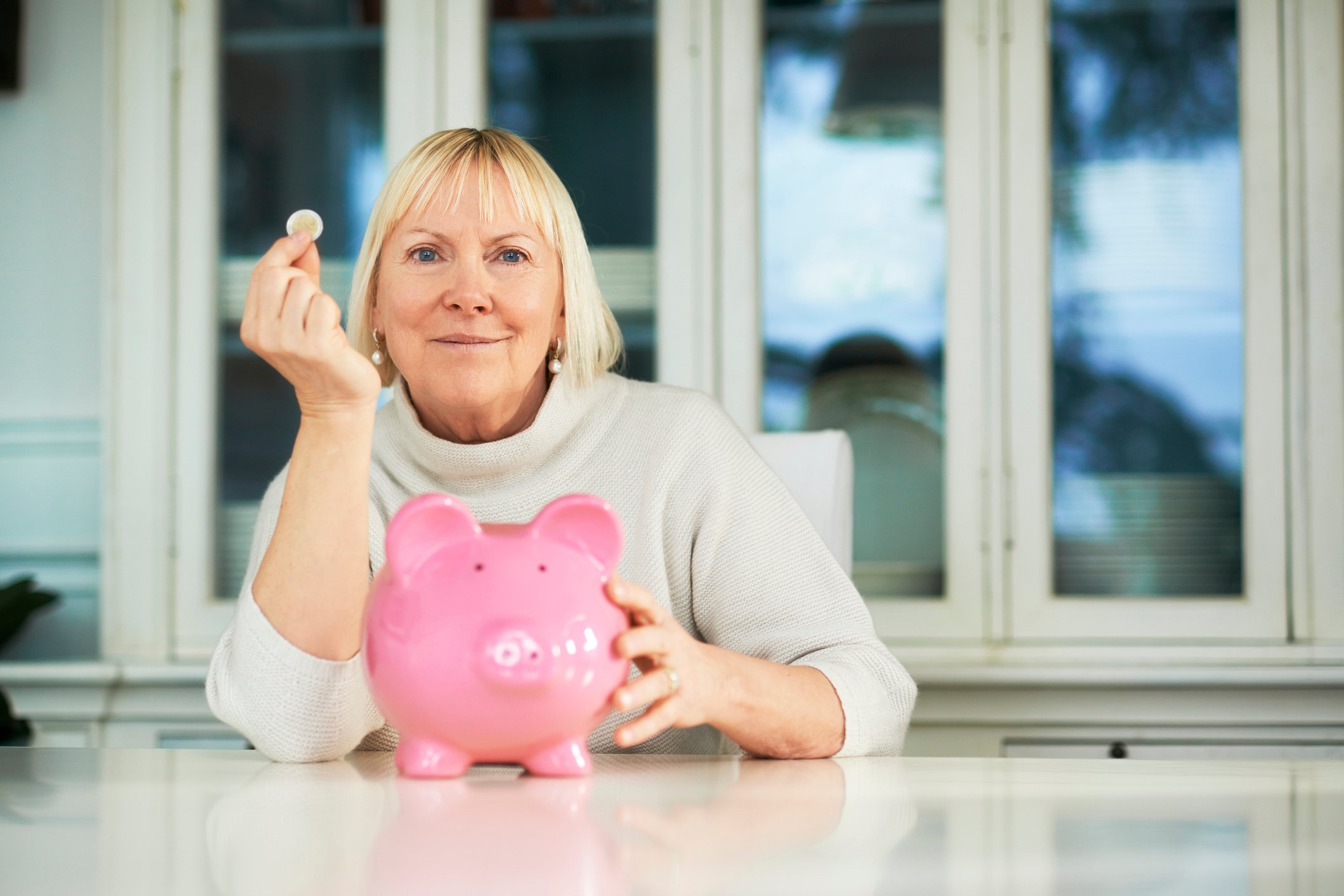 A woman holding up a coin by a piggy bank.