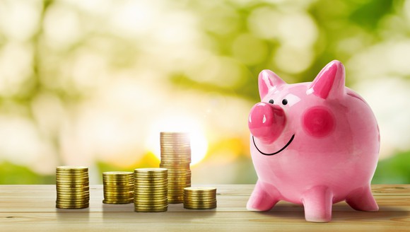 Stacks of gold coins next to a smiling piggy bank.