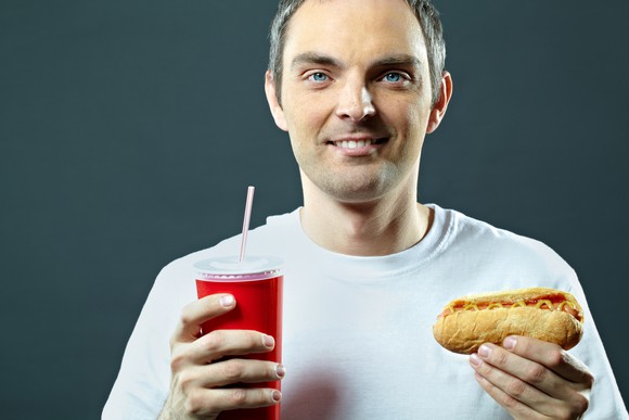 A man holds a hot dog and a soda