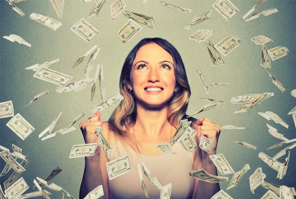 A woman stands in a shower of cash.