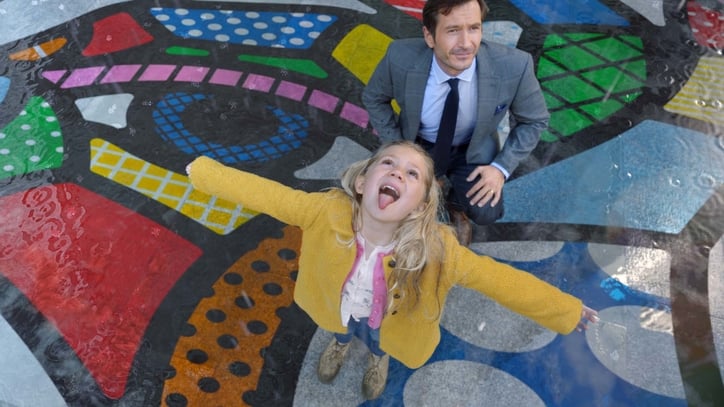 Young girl in colorful park opening her mouth to catch falling raindrops.