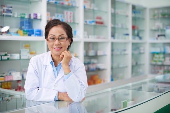 A pharmacist poses at a pharmacy counter.