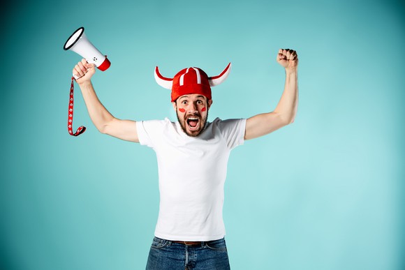 A sports fan raises his arms in celebration, holding a bullhorn in one hand.