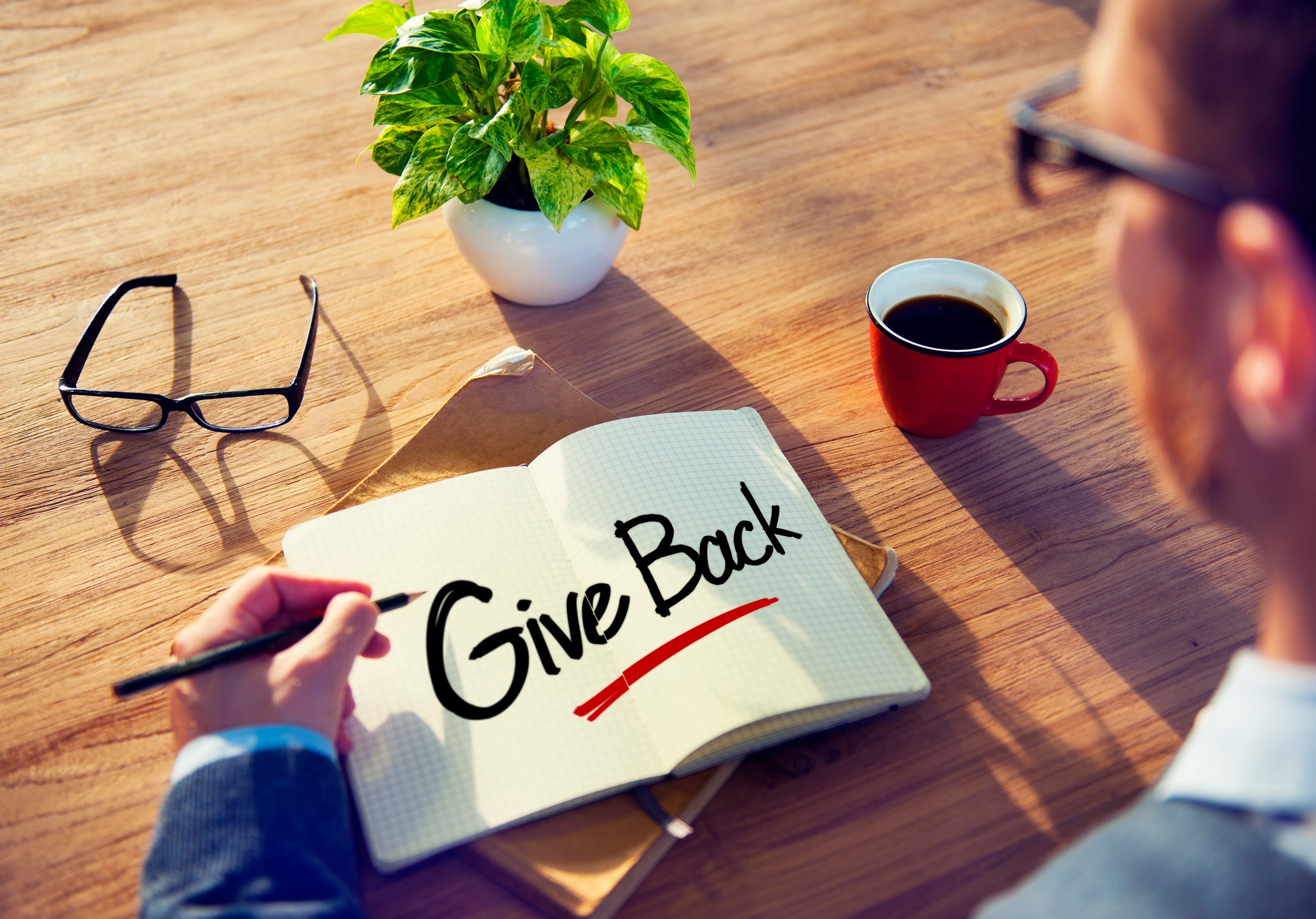 A person writing the words "give back" in a book.