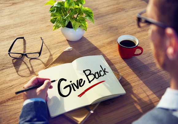A person writing the words "give back" in a book.