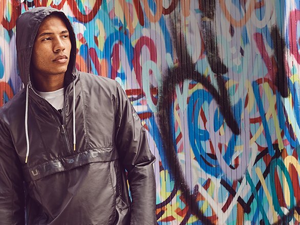 A model sporting an Under Armour windbreaker against a graffitied background.