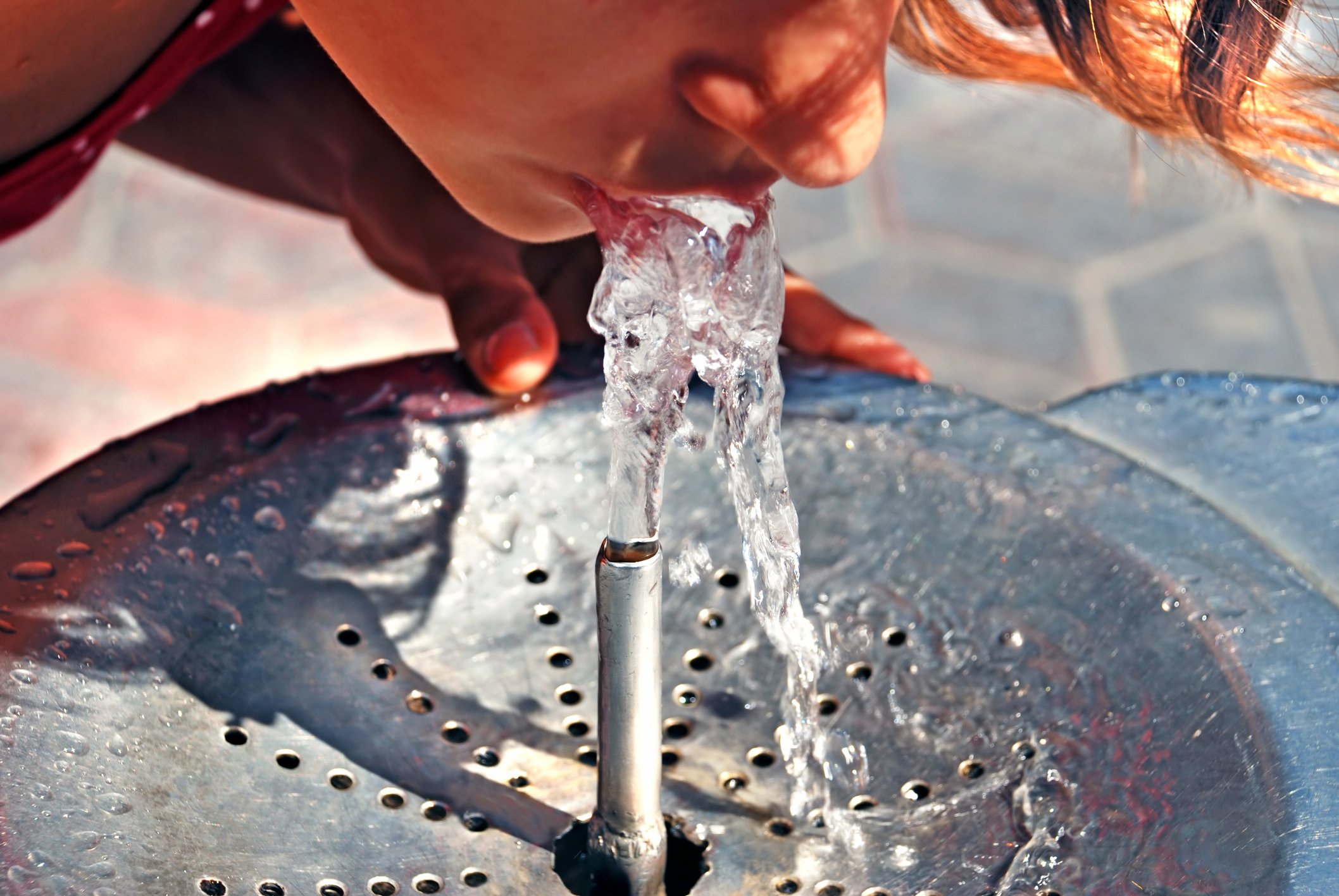 Young person drinking from a water fountain.