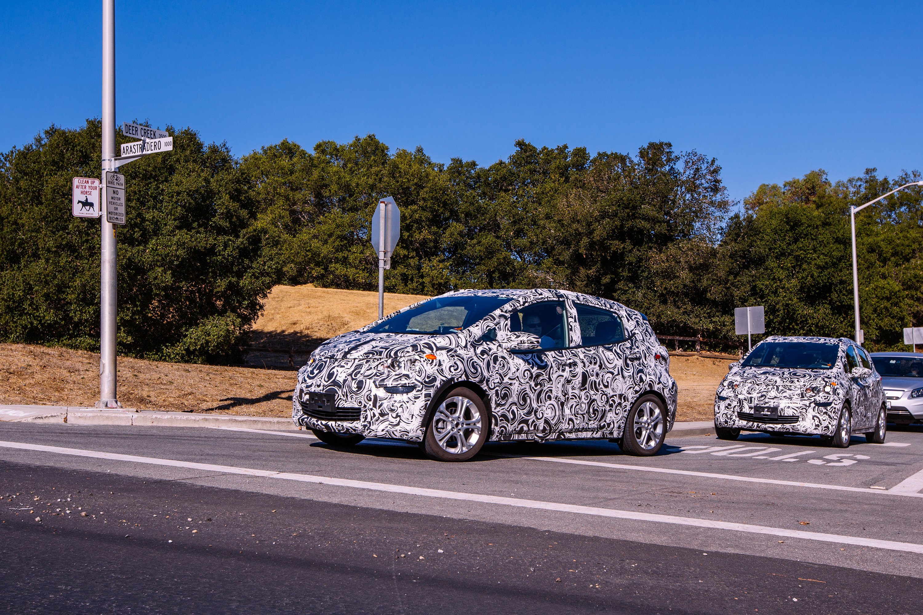 Two Chevrolet Bolt EVs in camouflage are shown testing on public roads in Palo Alto, California, near Tesla's headquarters. 