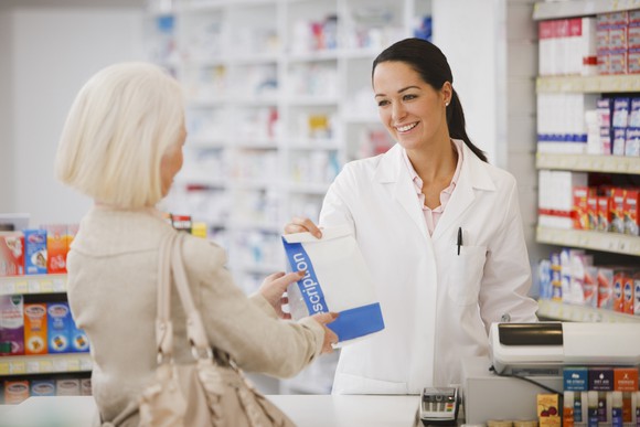 A pharmacist hands a bag containing a prescription to a customer.