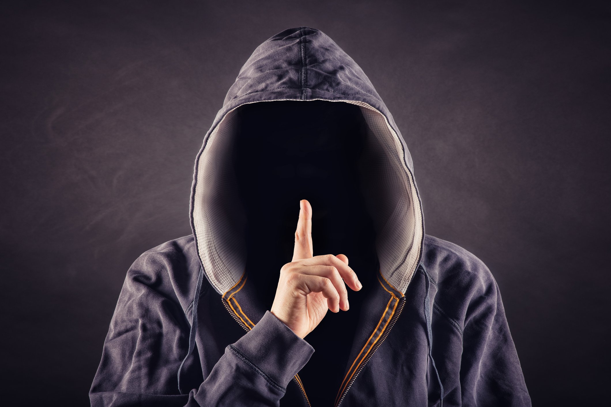 A hooded person holding his finger over his lips