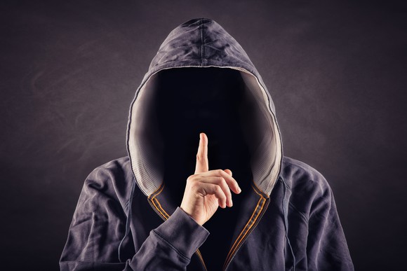 A hooded person holding his finger over his lips