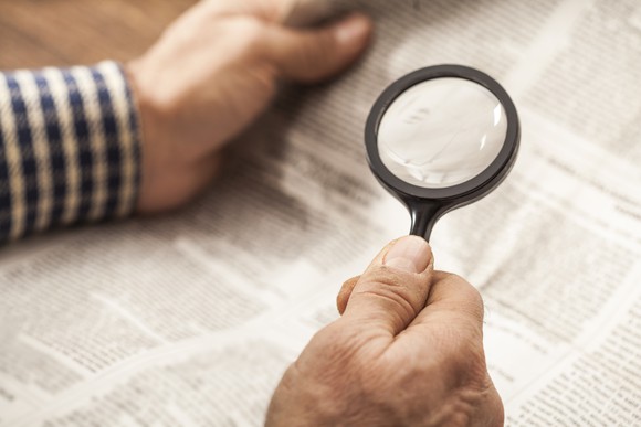 Man reading a newspaper with a magnifying glass.