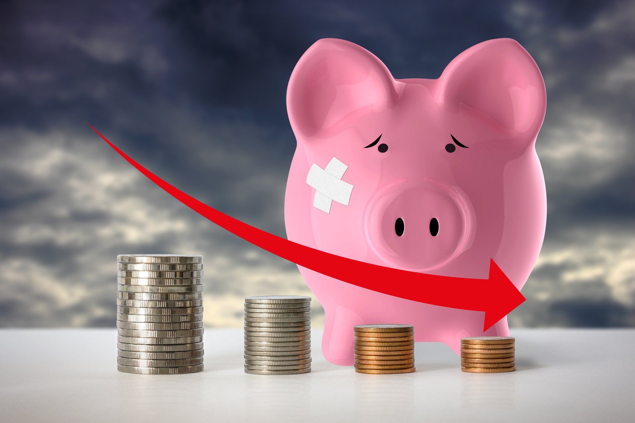 Bruised piggy bank standing behind four piles of coins progressing getting smaller. 