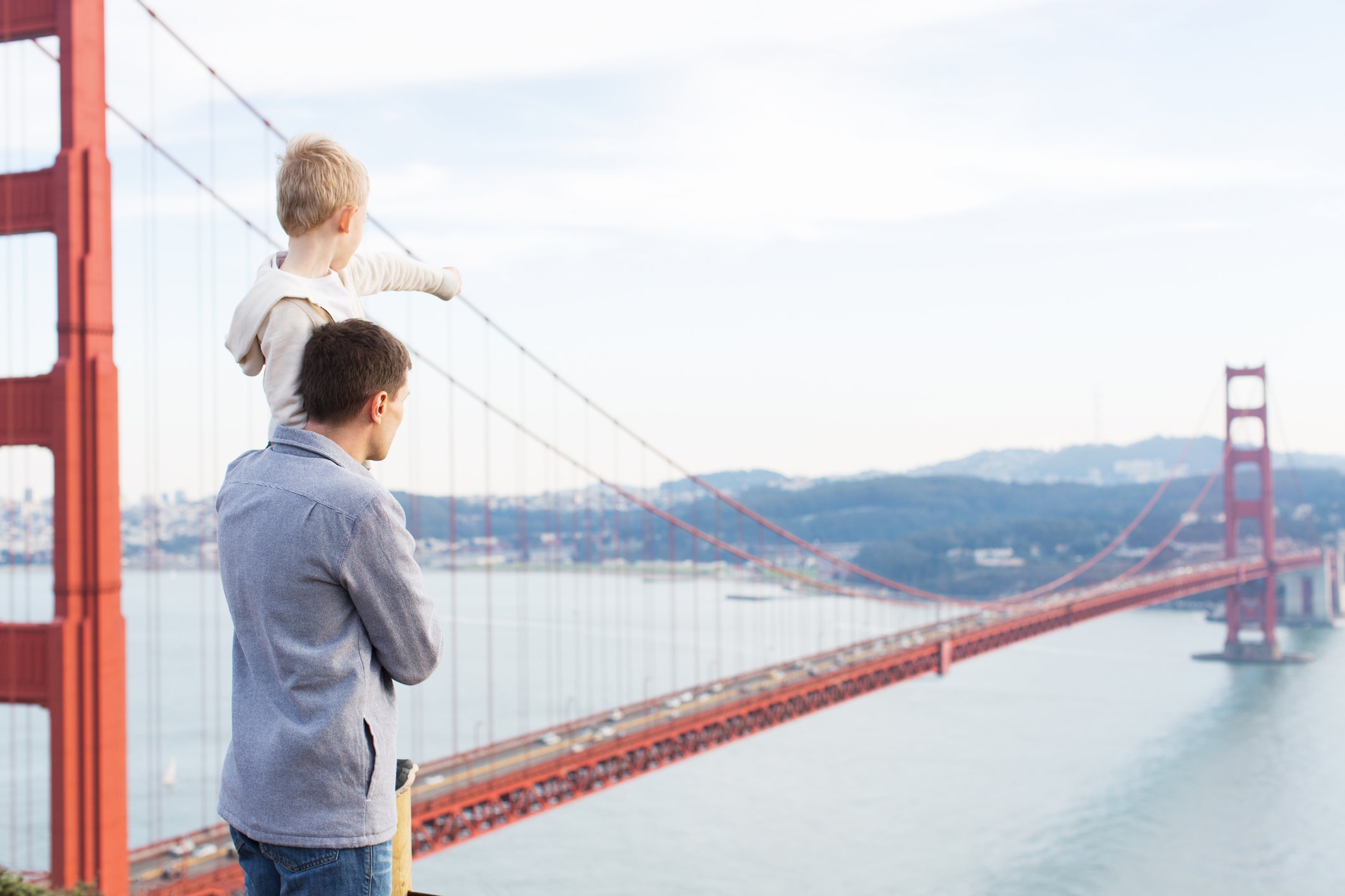 A man holds up a child, who points in the direction of the Golden Gate Bridge.