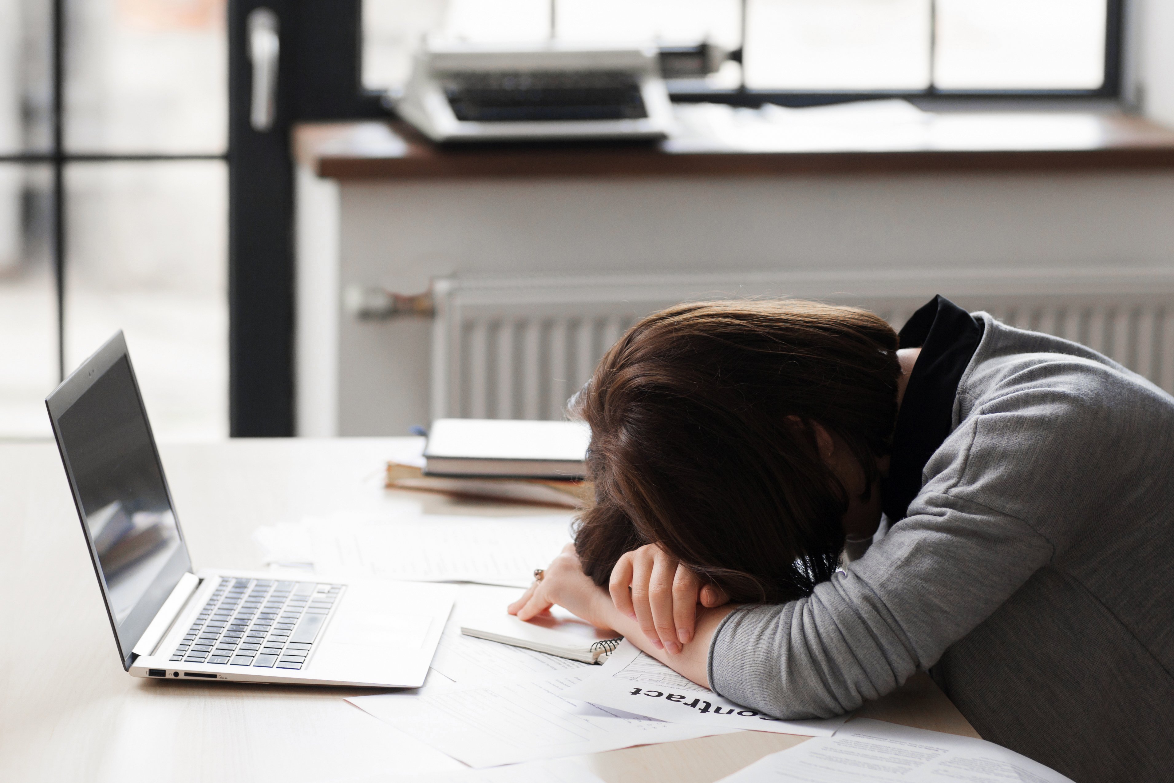 A woman puts her head down on her desk. 