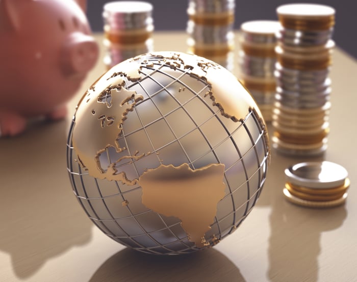 A globe sits in front of gold coins and a piggy bank.