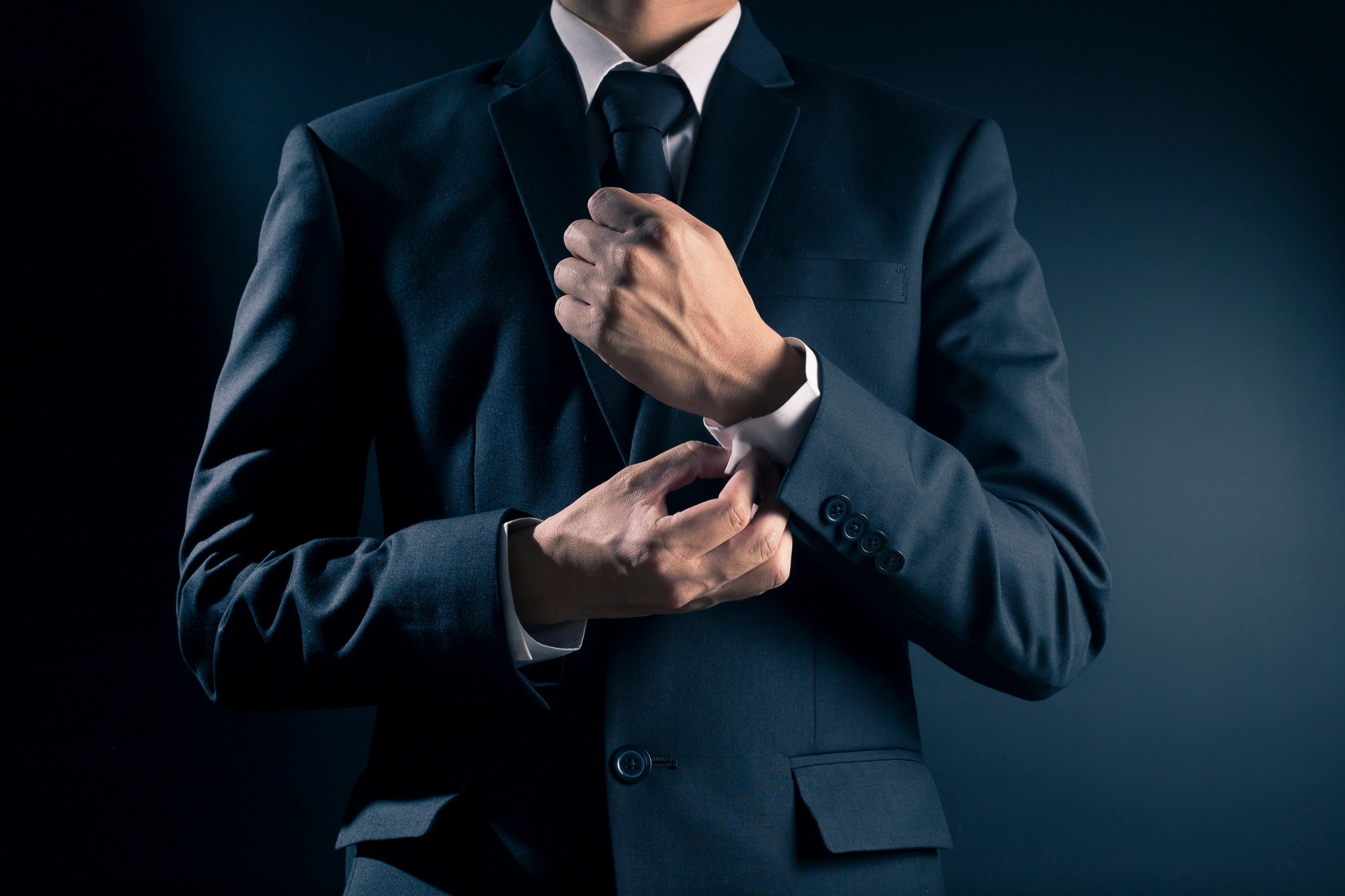 A man in a sut fixes his cuff.