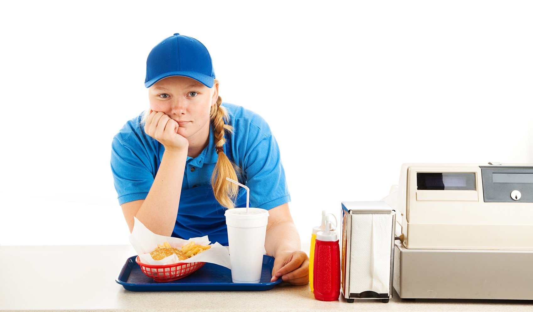 A frustrated-looking fast-food worker in a blue shirt and ball cap leans on the counter with her chin resting on the palm of her hand. Next to her are a cash register, a napkin dispenser, and condiments. In front of her is a tray with a fast-food order on it.